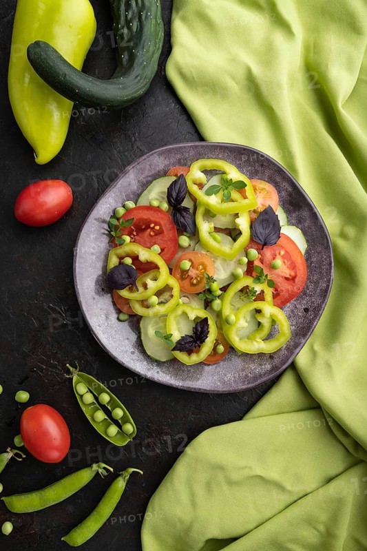 Vegetarian salad from green pea, tomatoes, pepper and basil on a black concrete background and green textile. top view, close up, flat lay