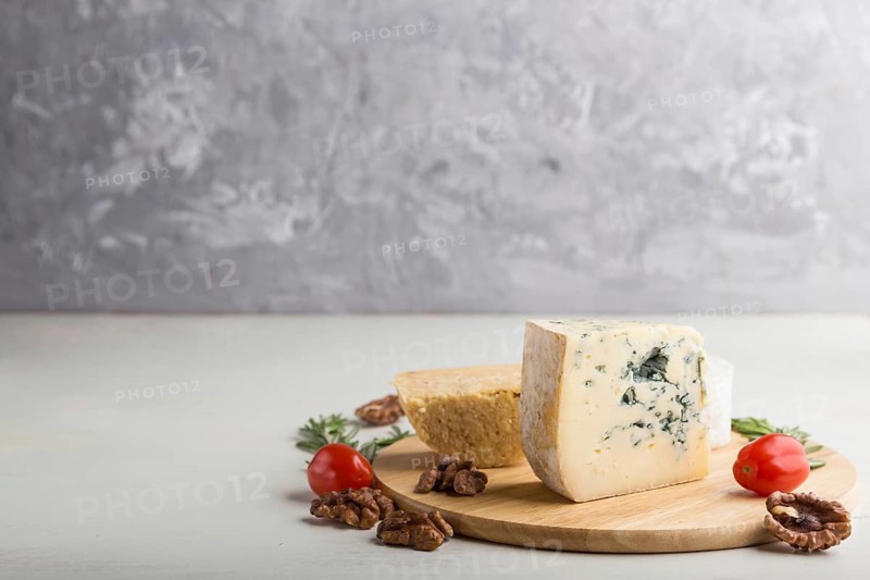 Blue cheese and various types of cheese with rosemary and tomatoes on wooden board on a white and gray background. Side view, copy space, selective focus