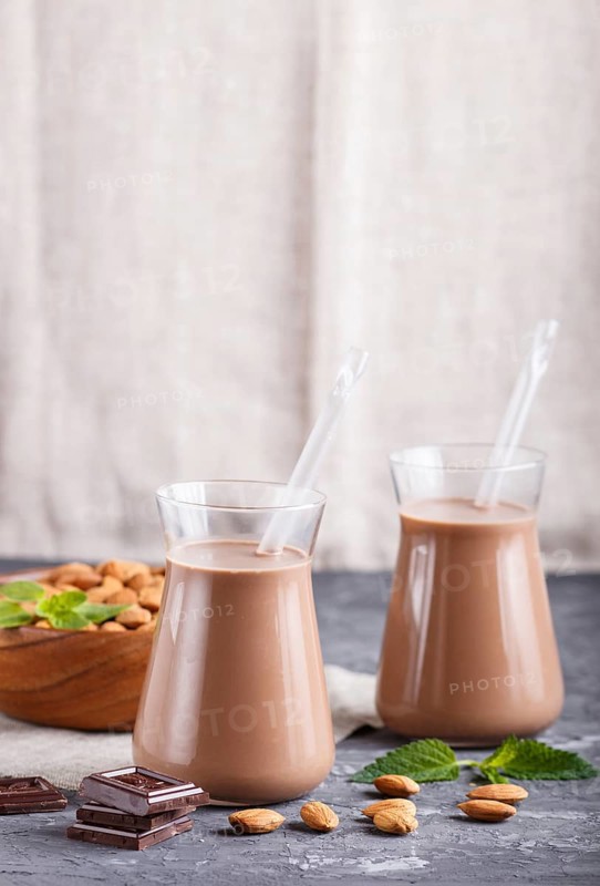 Organic non dairy almond chocolate milk in glass and wooden plate with almond nuts on a black concrete background. Vegan healthy food concept, close up, side view, copy space
