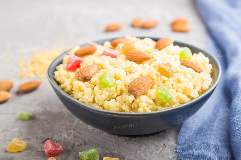 Millet porridge with candied fruits and almonds in blue ceramic bowl on a gray concrete background and blue linen textile. Side view, close up, selective focus