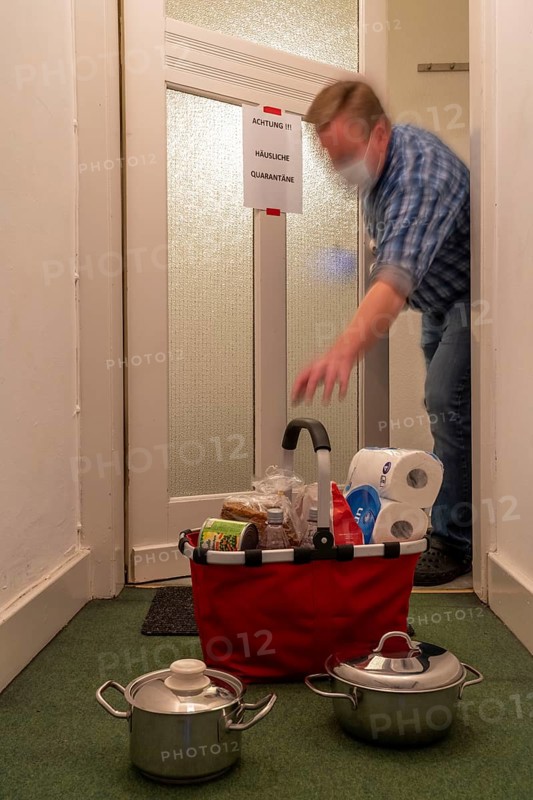 Symbolic image Domestic quarantine, man is in isolation at home due to a suspected corona infection, warning sign for visitors on the front door, communicates with a visitor through the door, neighbours have been shopping, cooked and put the things in front of the door