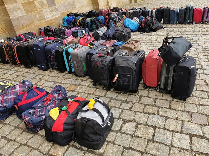 Luggage and rucksacks of different colours and sizes neatly lined up on a paved floor