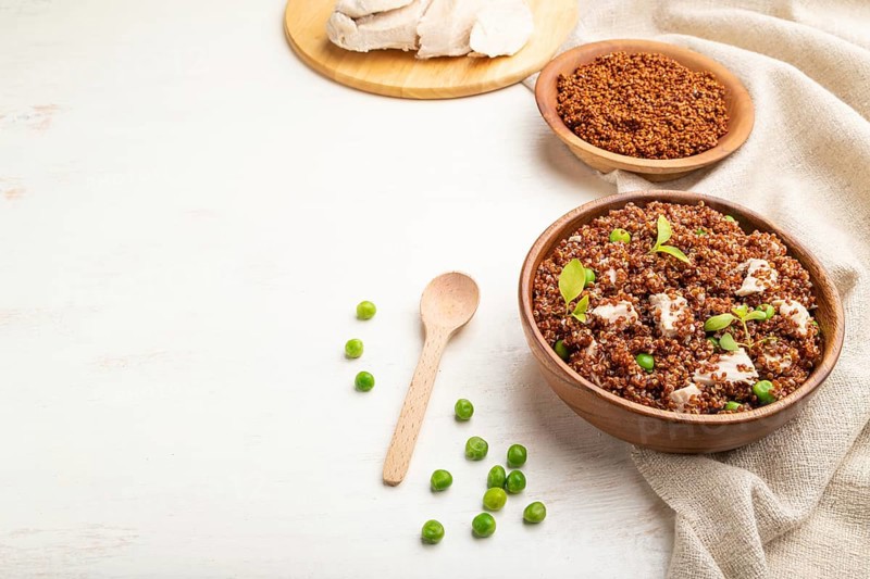 Quinoa porridge with green pea and chicken in wooden bowl on a white wooden background and linen textile. Side view, close up, copy space