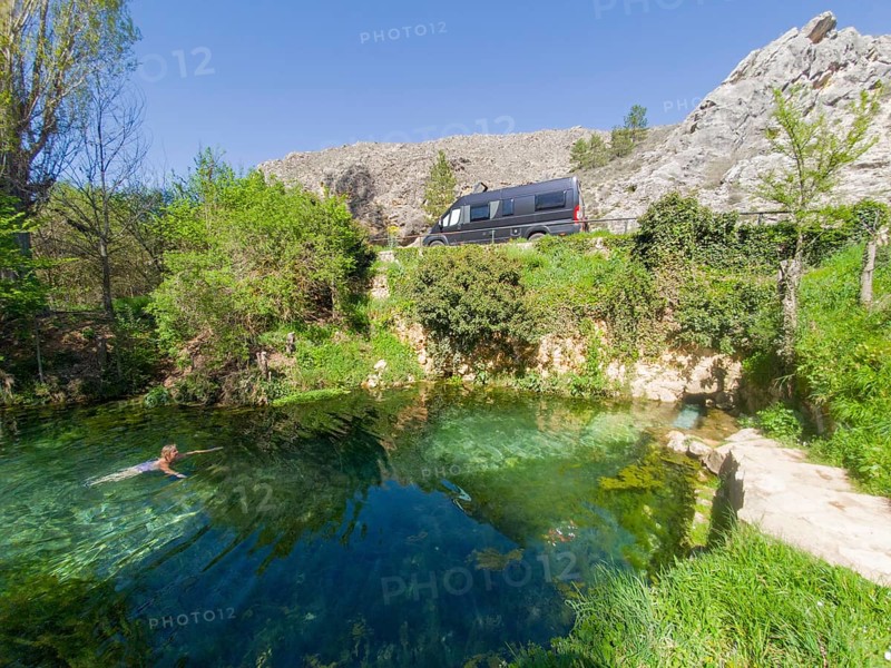 Eine Person schwimmt in einer klaren Quelle in den Bergen neben einem parkenden Van an einem sonnigen Tag, Wohnmobil, natürliche warme Quelle, Fuente de la Salud, am Fluss Duratón, Sepúlveda, Sepulveda, Segovia, Kastilien und León, Spanien