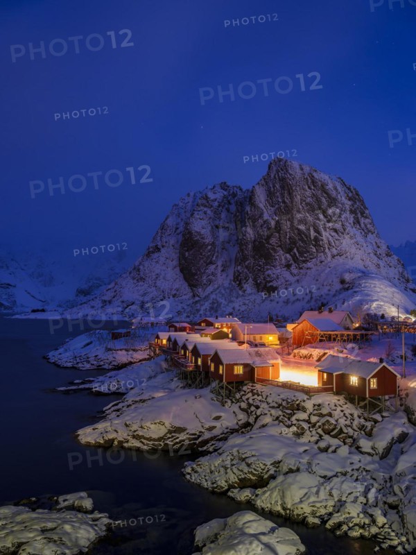 Rorbuer huts of Hamnoy at the fjord at dusk, snowy mountains in the background, Hamnøy, Reine, Moskenesøya, Lofoten, Norway, Europe