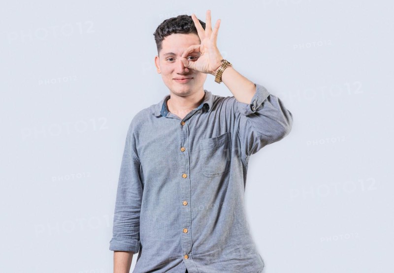 Smiling person making ok gesture looking through fingers isolated. Happy young man making ok gesture with hand looking through fingers