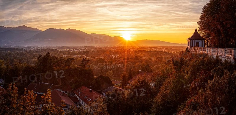 A picturesque sunset over an autumnal landscape with mountains and a building in the foreground, Neubeuern