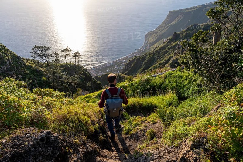 Young man looking out to sea on cliff, evening mood, green coastal landscape on cliff, sea and coast, viewpoint Miradouro da Raposeira, Paul do Mar, Madeira, Portugal, Europe