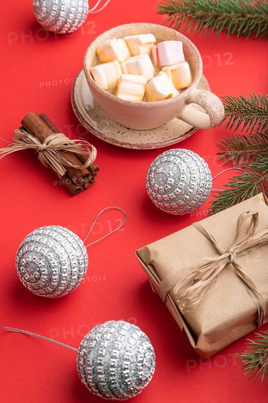Christmas or New Year composition. Decorations, box, cinnamon, silver balls, fir and spruce branches, cup of coffee, on a red paper background. Side view, close up