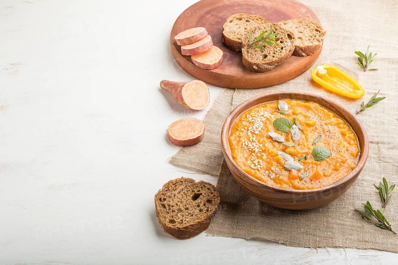 Sweet potato or batata cream soup with sesame seeds in a wooden bowl on a white wooden background with linen textile. side view, close up, copy space