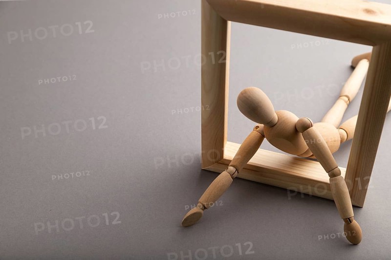 Wooden mannequin crawl out of a wooden frame on gray pastel background. escape, break rules, freedom, depression concept. copy space
