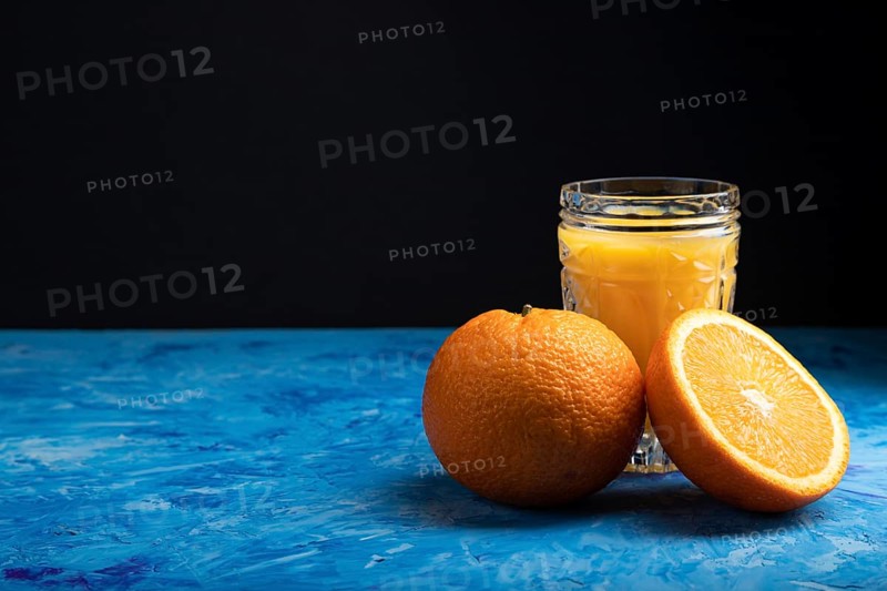Glass of orange juice on a black and blue background. Hard light, contrast. Side view, copy space