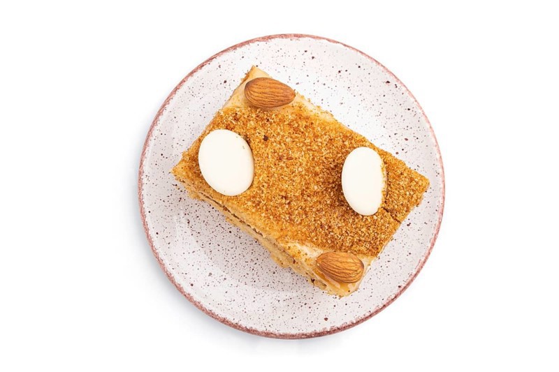 Honey cake with milk cream, caramel, almonds isolated on a white background. Top view, flat lay, close up