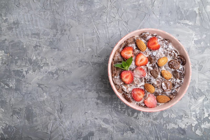 Chocolate cornflakes with milk, strawberry and almonds in ceramic bowl on pastel orange background. Top view, flat lay, copy space