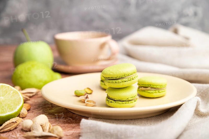 Green macarons or macaroons cakes with cup of coffee on a brown concrete background and linen textile. Side view, close up, selective focus