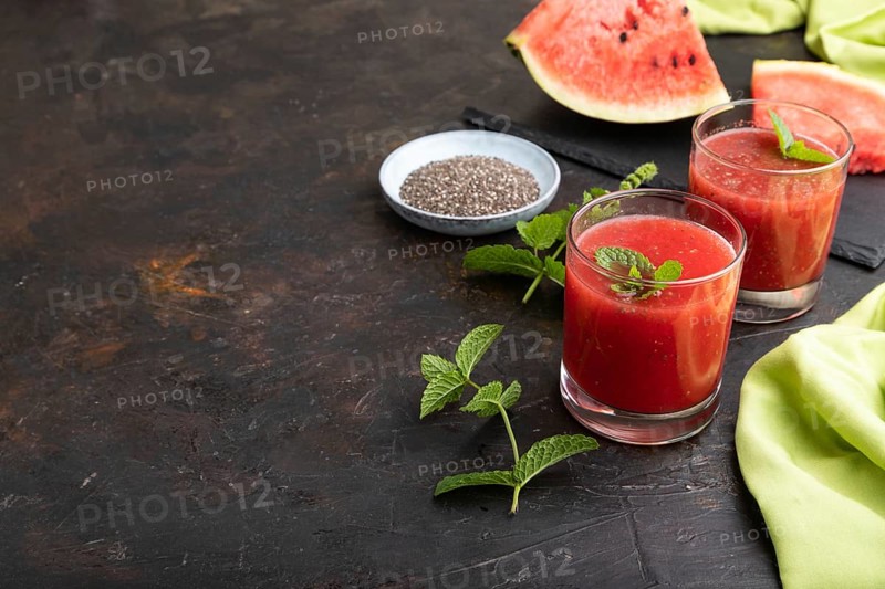 Watermelon juice with chia seeds and mint in glass on a black concrete background with green textile. Healthy drink concept. Side view, copy space