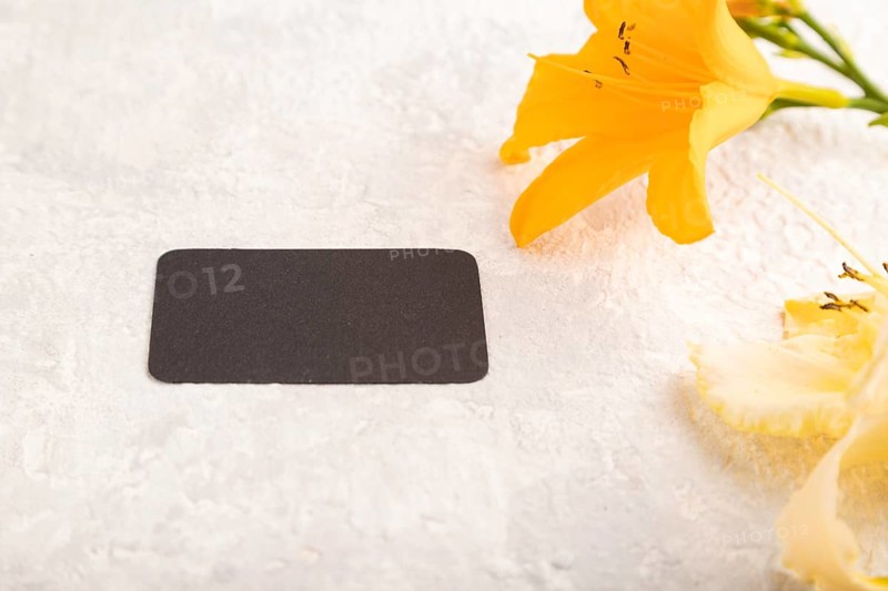 Black paper business card mockup with orange day-lily flower on gray concrete background. Blank, side view, copy space, still life. spring concept