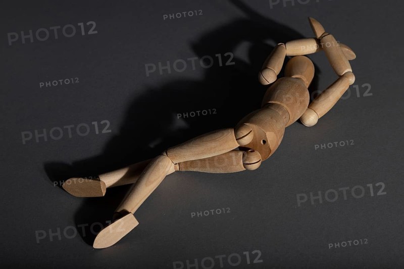 Wooden mannequin lies in a protective position on gray background. loneliness, violence, vulnerability, depression disorder concept. copy space, hard light