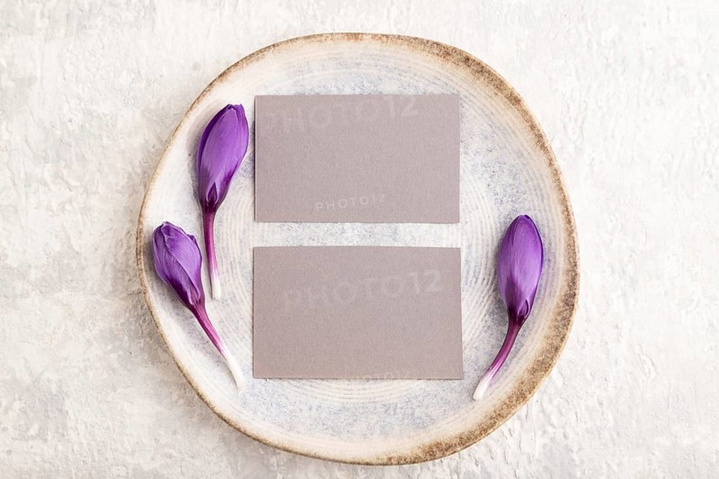 Gray paper invitation card, mockup with crocus flowers on ceramic plate and gray concrete background. Blank, flat lay, top view, still life, copy space, wedding invitation
