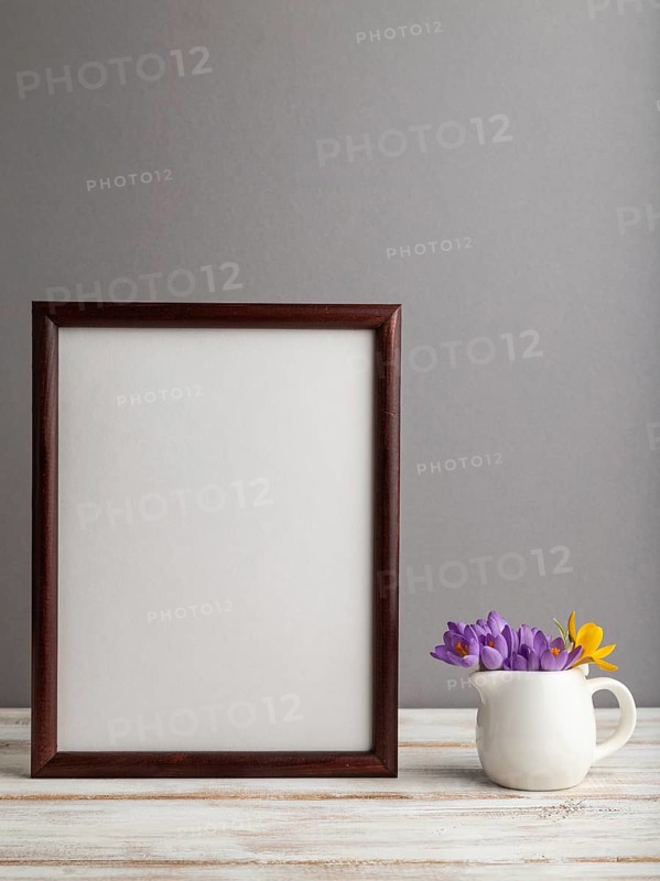 Brown wooden frame mockup with snowdrop crocus flowers on gray paper background. Blank, vertical orientation, still life, copy space