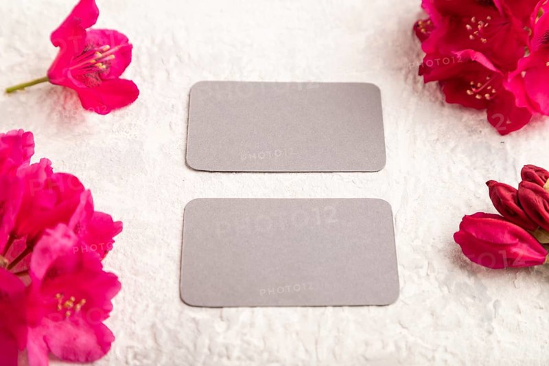 Gray business card with purple azalea flowers on gray concrete background. side view, copy space, mockup, template, spring, summer minimalism concept