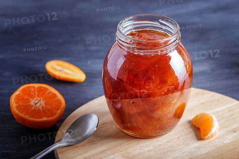 Tangerine and kumquat jam in a glass jar with fresh fruits on a black wooden table. Homemade, copy space, close up
