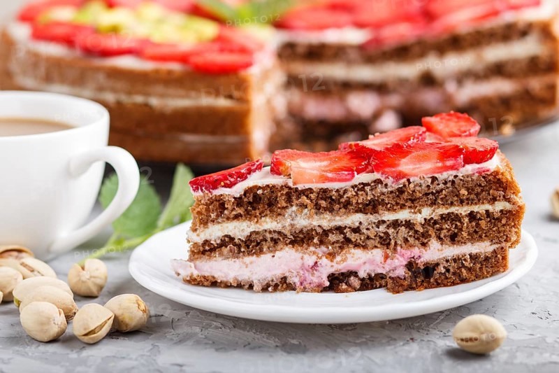 Homemade cake with yoghurt cream, strawberry, pistachio and a cup of coffee on a gray concrete background. side view, selective focus, close up