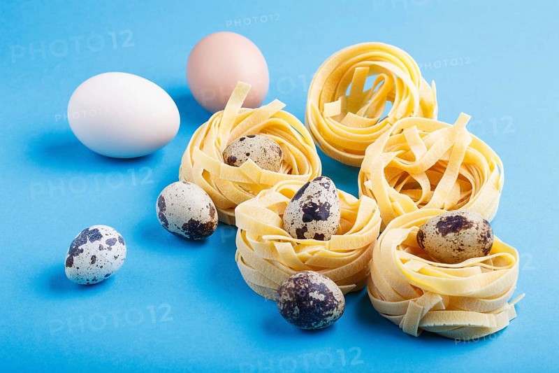 Raw uncooked tagliatelle pasta with quail eggs on a blue pastel background. side view, close up
