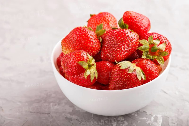 Fresh red strawberry in white bowl on gray concrete background. side view, close up, selective focus