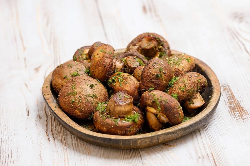 A variety of freshly picked mushrooms is beautifully arranged on a rustic wooden plate, sprinkled with herbs, showcasing their earthy tones.