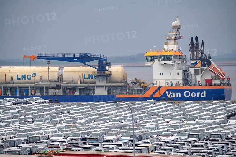 Parking space for import vehicles, hundreds of Hyundai Ioniq, electric cars, waiting for onward transport, behind them, on the Weser, the dredger, the hopper dredger, suction dredger, Vox Ariane, which holds the tug to a certain depth, at the EUROGATE container terminal in the overseas port of Bremerhaven, Lower Saxony, Germany, Europe