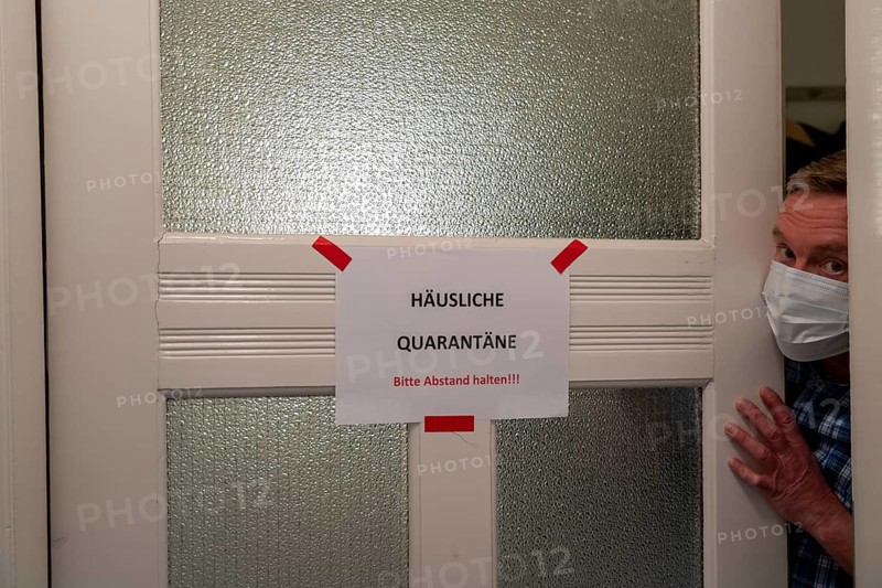 Symbolic image Domestic quarantine, man is in isolation at home due to a suspected corona infection, warning sign for visitors on the front door, communicating with a visitor through the door