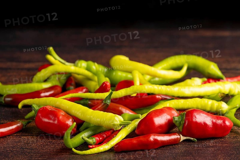 A mixture of green and red peppers lies on a dark wooden surface, food photography