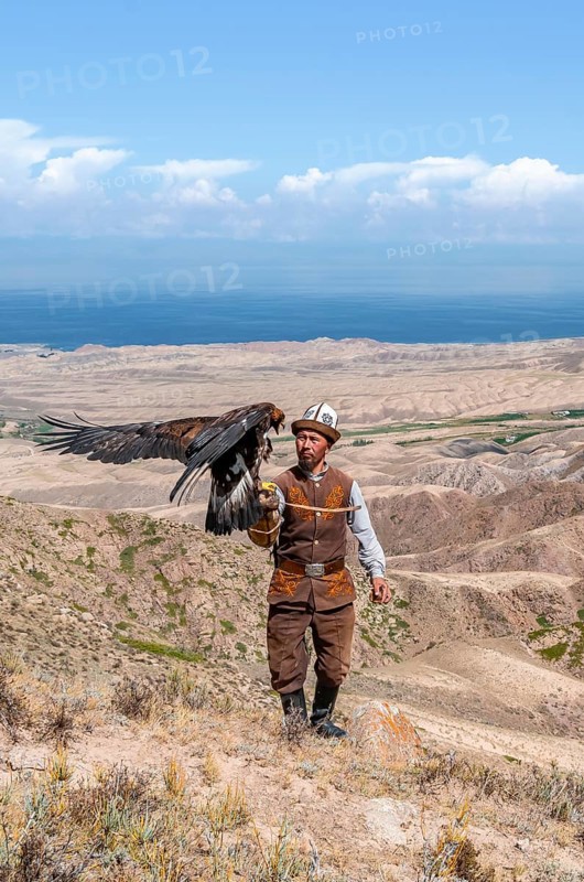 Traditional Kyrgyz eagle hunter hunting in the mountains in a dry landscape, near Kysyl-Suu, Issyk Kul, Kyrgyzstan, Asia