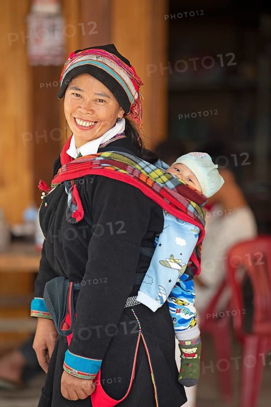 Vietnamese woman, 43 years old, in traditional traditional costume of the Dao minority, carrying her son, 3 months, on her back, Nam Dam Dao Cultural Village, Ha Giang province, Vietnam, Asia