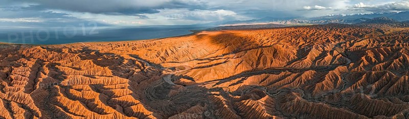 Panorama, landscape of eroded hills, badlands at sunset, behind Issyk Kul Lake and mountain peaks of the Tien Shan Mountains, aerial view, Canyon of the Forgotten Rivers, Issyk Kul, Kyrgyzstan, Asia