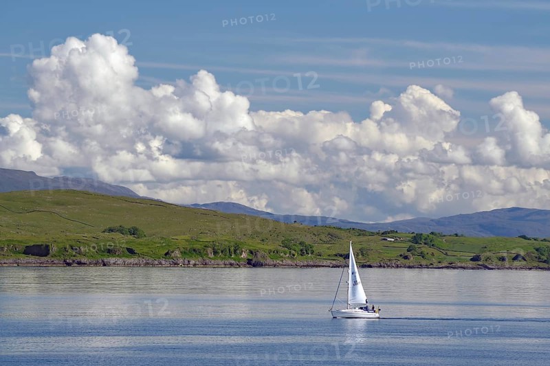 Lone sailing boat on calm water, surrounded by vast nature and mountains under a cloudy sky, ferry Oban, Mull, Scotland, United Kingdom, Europe