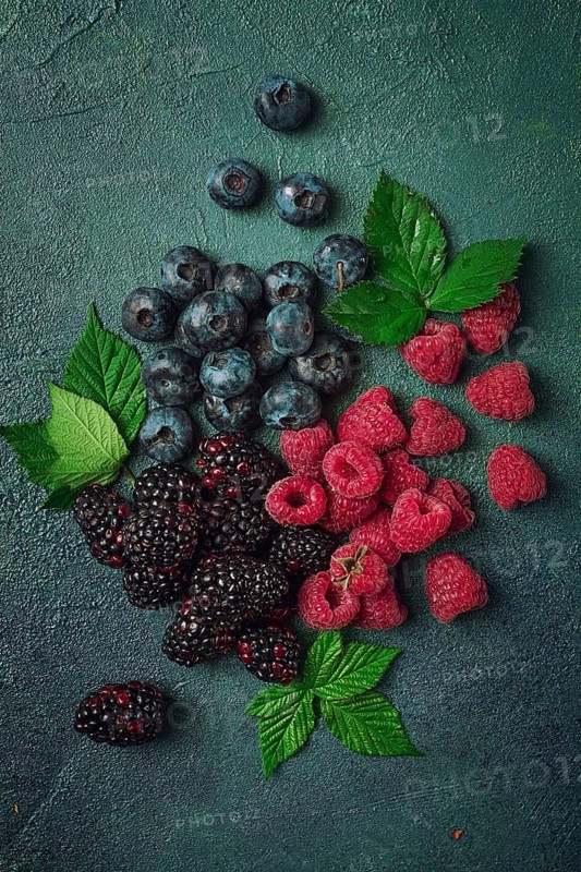 A mix of ripe berries, with leaves scattered on the table, raspberries, blackberries, blueberries, food background