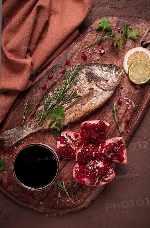 Fried dorado fish, with spices and herbs, on a wooden board, pomegranate sauce, close-up, no people