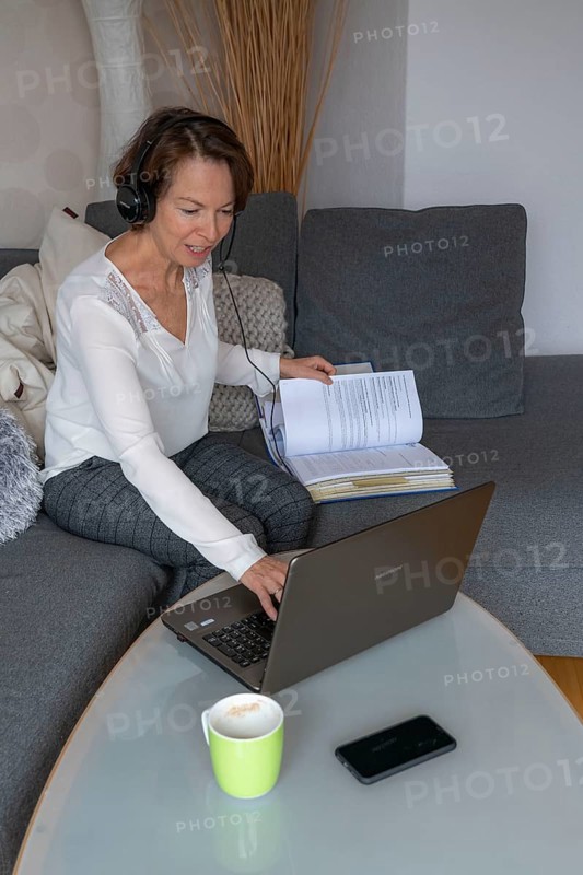 Woman, mid-50s, works from home, with laptop and communicates with colleagues via headset, home office, on the sofa