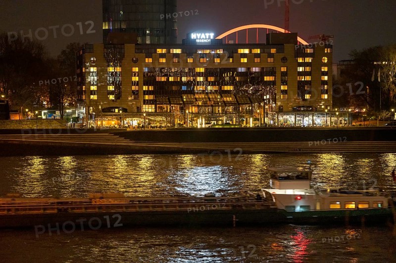 The Hyatt Regency Hotel on the Rhine, in Cologne Deutz, behind it the illuminated arch of the Lanxess Arena, cargo ship on the Rhine, North Rhine-Westphalia, Germany, Europe