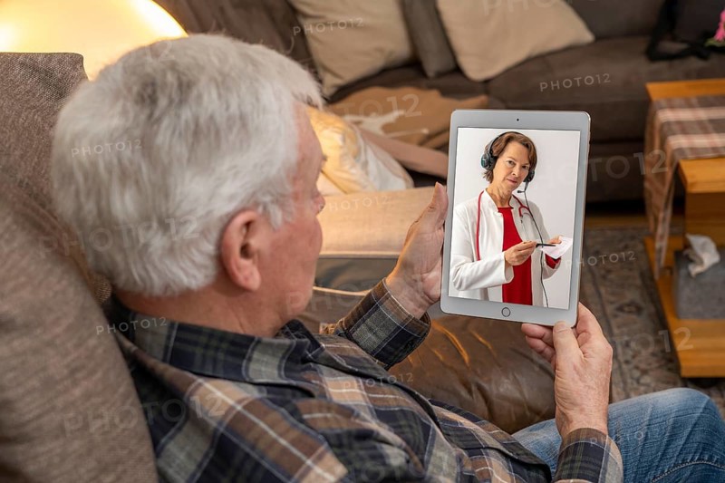 Symbolic image of telemedicine, elderly patient speaking to a doctor in a video conference from home