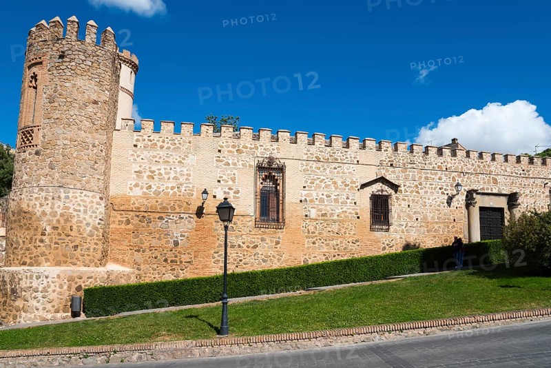 Medieval castle with stone walls and a tower, surrounded by grass and road under a blue sky, Palace of the Dukes of Maqueda, Palacio de los Duques de Maqueda, Palacio de la Cava, Toledo, Castilla-La Mancha, Spain, Europe