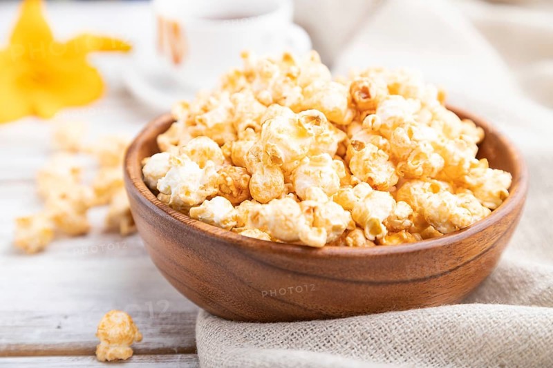 Popcorn with caramel in wooden bowl and a cup of coffee on a white wooden background and linen textile. Side view, close up, selective focus