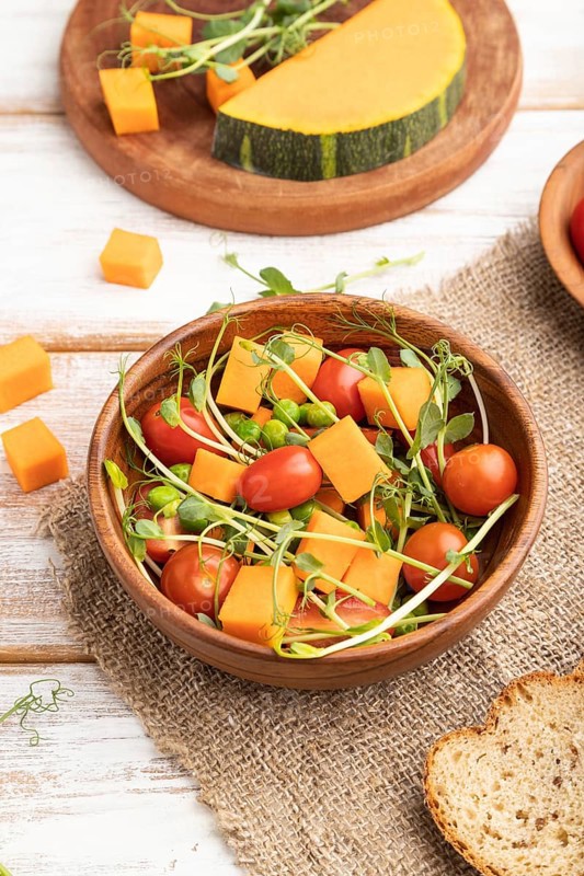 Vegetarian vegetable salad of tomatoes, pumpkin, microgreen pea sprouts on white wooden background and linen textile. Side view, close up