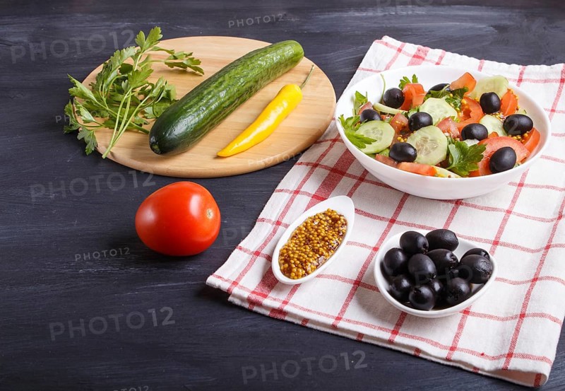 Vegetarian salad of tomatoes, cucumbers, parsley, olives and mustard on linen tablecloth and black wooden background, close up