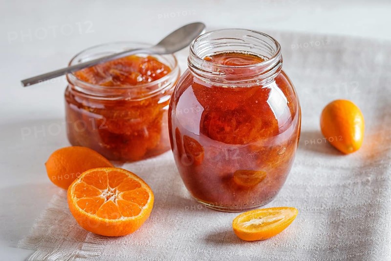 Tangerine and kumquat jam in a glass jar with fresh fruits on white background. Homemade, close up