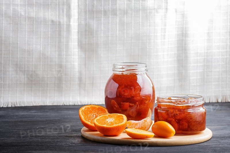 Tangerine and kumquat jam in a glass jar on a black wooden table and white linen background. Homemade, copy space