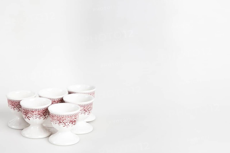 A set of white and red ceramic egg cups with a floral pattern arranged on a light-coloured background, copy space