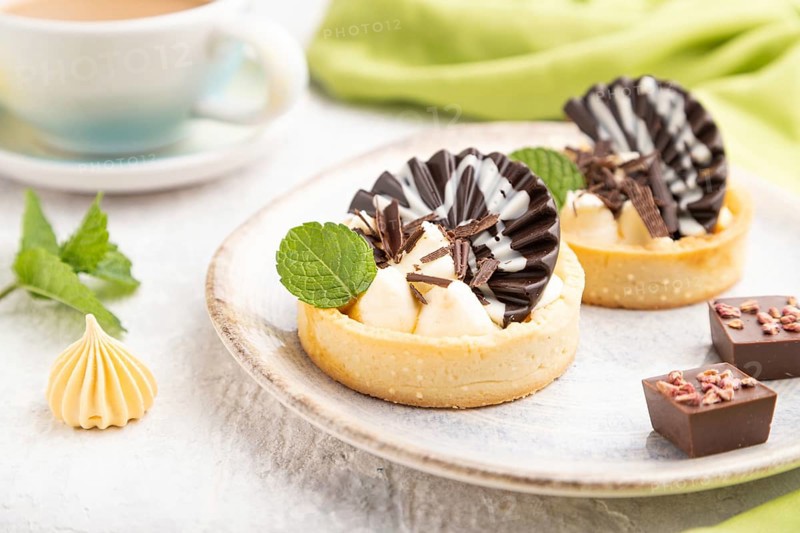 Sweet tartlets with chocolate and cheese cream with cup of coffee on a gray concrete background and green textile. Side view, close up, selective focus
